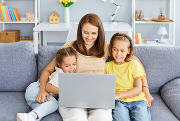 Happy family of mother or babysitter, cute little kids children enjoy using laptop watching cartoons, internet video call or shopping online looking at computer screen sitting together on sofa at home