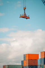 A large industrial crane hook and spreader lifting mechanism is suspended in the air against a...