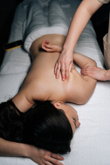 Close-up top view of unrecognizable massage therapist providing soothing back treatment to female client lying on massage table, delivering stress-relief wellness services in serene spa environment.
