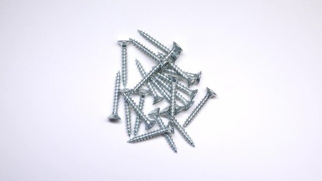 A collection of uniformly sized silver screws with sharp threads and flat countersunk heads arranged on a clean white background.