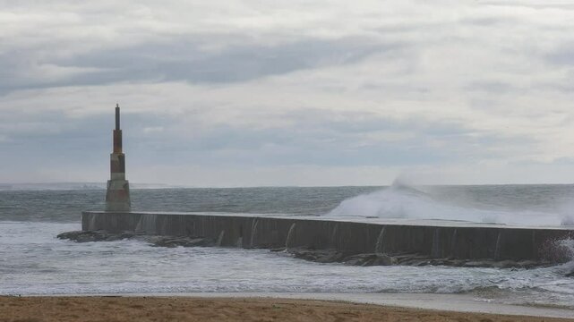 Huge waves crushing over Breakwater during winter storm Atlantic waves washing the lighthouse on Praia da Aguda sandy beach at Aguda settlement near Porto, Portugal.