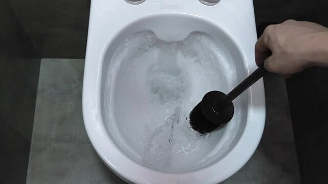 Professional janitor thoroughly cleaning white ceramic toilet bowl, scrubbing interior surfaces with black plastic brush to eliminate stubborn dirt and persistent grime. slow motion