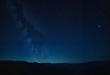 Naklejka premium Endless starry night sky with countless twinkling stars, deep blue and black shades, blurred distant horizon background, tranquil and mesmerizing atmosphere