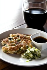 Korean seafood pancake with soy dipping sauce and glass of wine on wooden table