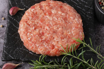 Fresh ground meat patty ready for cooking with herbs and garlic on a dark plate