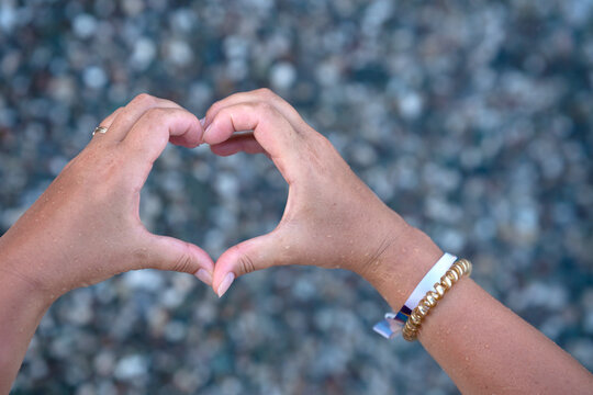 Two hands form a heart shape against a blurred natural background with grey pubbles