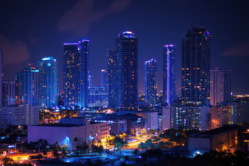 Obraz premium Vibrant city skyline illuminated in neon lights under a night sky, showcasing modern skyscrapers and colorful urban architecture.