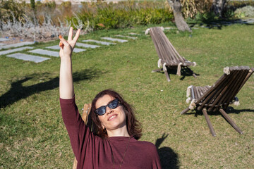 Woman lying on a deck chair, showing victory or peace sign, enjoying the sun in a garden