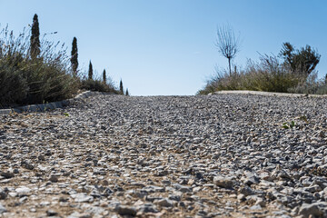 Low angle view of a gravel road climbing a hill in the countryside with vegetation and trees on the sides