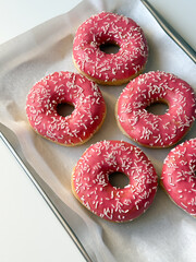 Donuts with pink glaze on metal tray top view close up