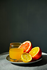 Glass of fresh citrus juice and half cut fruit on the plate.