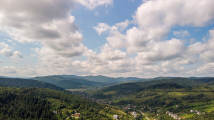 Obraz premium Majestic Mountains, Lush Green Forests, And Soft White Clouds On A Sunny Day. Aerial View Showcasing The Stunning Beauty Of Nature From A High Perspective. 