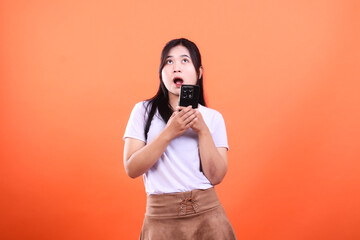 Obraz premium Woman with open mouth looking up while holding a phone isolated on orange
