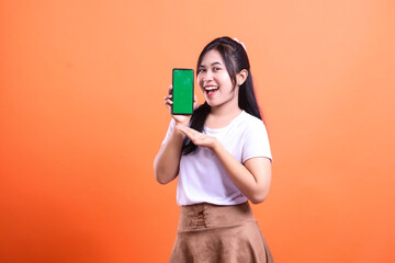 Naklejka premium Young Woman Presenting a Smartphone with Green Screen on Orange Background