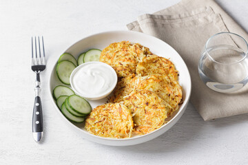 Crispy cabbage pancakes with sour cream and fresh cucumber slices on white plate