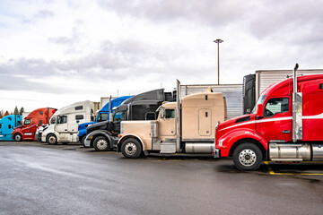 Different makes and models of the big rig semi trucks with semi trailers standing in row on truck...