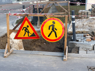 Warning signs indicate active construction in an urban environment, showing a pedestrian path diversion and work area. Gravel and earth are exposed, reflecting ongoing repairs