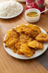 Crispy fried patacones served on a table with a portion of rice and spicy hot sauce, perfect for food, cuisine, and traditional dish-themed content.