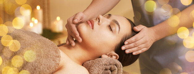 Beautiful young woman receiving face massage in spa salon, bokeh effect. Banner design