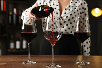 Professional sommelier pouring red wine into glasses at wooden table indoors, closeup