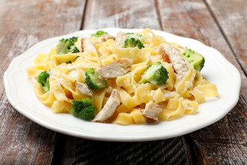 Delicious pasta Alfredo with chicken, cheese and broccoli on wooden table, closeup