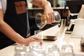 Barista pouring coffee from glass coffeemaker into cup at table in cafe, closeup