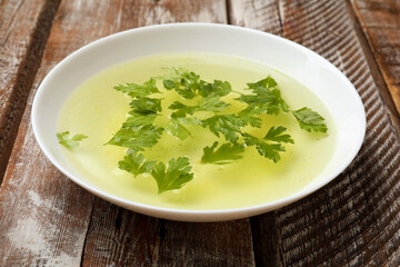 Tasty chicken bouillon with parsley in bowl on wooden table, closeup