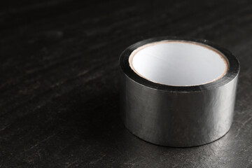 Roll of silver adhesive tape on black table, closeup. Space for text