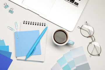 Designer's workplace with stationery, color palettes, cup of coffee and laptop on grey table, flat...