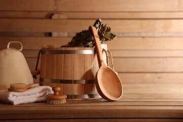 Bucket, whisk, massaging brushes and other equipment on wooden bench in sauna. Space for text