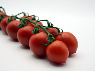 Isolated close-up of ten roma tomatoes (solanum lycopersicum) on a vine seen from an angle on white background. Concept: ingredients, healthy eating, cooking,