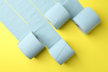 Light blue toilet paper rolls on yellow background, flat lay