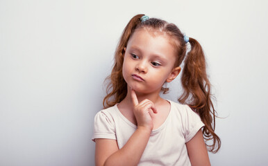 Happy fun cynical thinking kid girl with finger holding under the face looking down with empty copy...