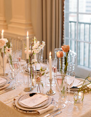Elegant dining setup with candles and floral centerpieces in a bright, airy room during daytime