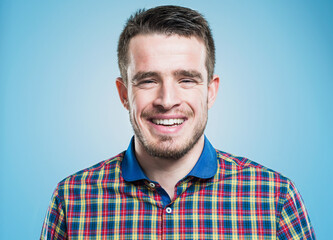 Fototapeta premium Happy man, portrait and laughing with studio for funny joke, expression or creative model on a blue background. Male person, beard and shirt with smile in joy for fashion, style or positive attitude