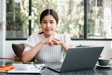 A young woman in a white sweater working on a laptop in a bright, modern home office setting.