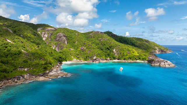 Prominent rocky shoreline surrounded by dense greenery, meeting the crystal-clear turquoise waters of the ocean. Seychelles, Mahe.