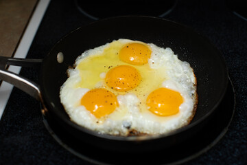 four almost fried eggs in cooking in a black pan on the stove