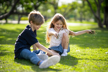 Fototapeta premium Outdoors portrait of two adorable children shares friendship. Two little girl and boy playing in the park. Two siblings having fun on sunlight and nature background. Childhood and friendship concept