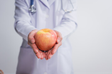 A male doctor stands holding an apple against a white background, promoting healthy eating educates...