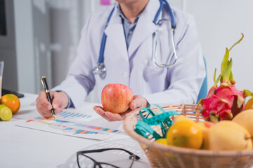 A male nutritionist works at his desk, discussing the benefits of eating fruit. He analyzes diets and educates patients on healthy eating habits for optimal health and well-being