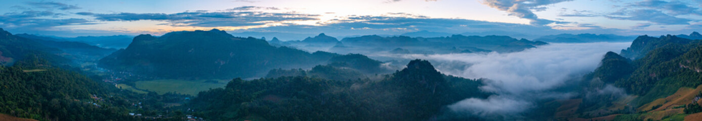 Fototapeta premium Aerial view A breathtaking view of dawn breaking over a misty mountain landscape, with layers of fog and vibrant colors painting the horizon. The serene atmosphere and natural beauty