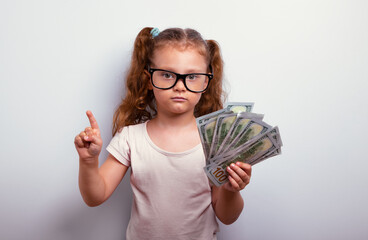 Happy thinking business kid girl in eye glasses holding the money, cash dollars in the hand  and...