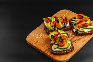 Vegan toast with avocado, cherry tomatoes, and balsamic glaze on wooden board