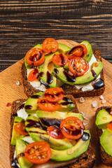 Delicious avocado and tomato toast served on wooden board for breakfast