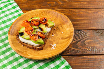 Delicious open-faced sandwich topped with tomatoes and avocado on wooden plate