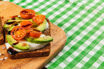 Delicious open-faced sandwich with fresh tomatoes and avocado on wooden board