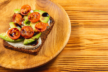 Delicious toast with fresh tomatoes and avocado on wooden plate