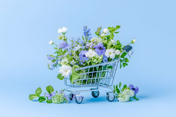 Spring flowers in mini shopping cart, blue background, floral shopping concept