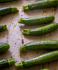 A tray of baby courgettes, or zucchinis, sprinkled with salt, pepper and olive oil, ready for roasting.
